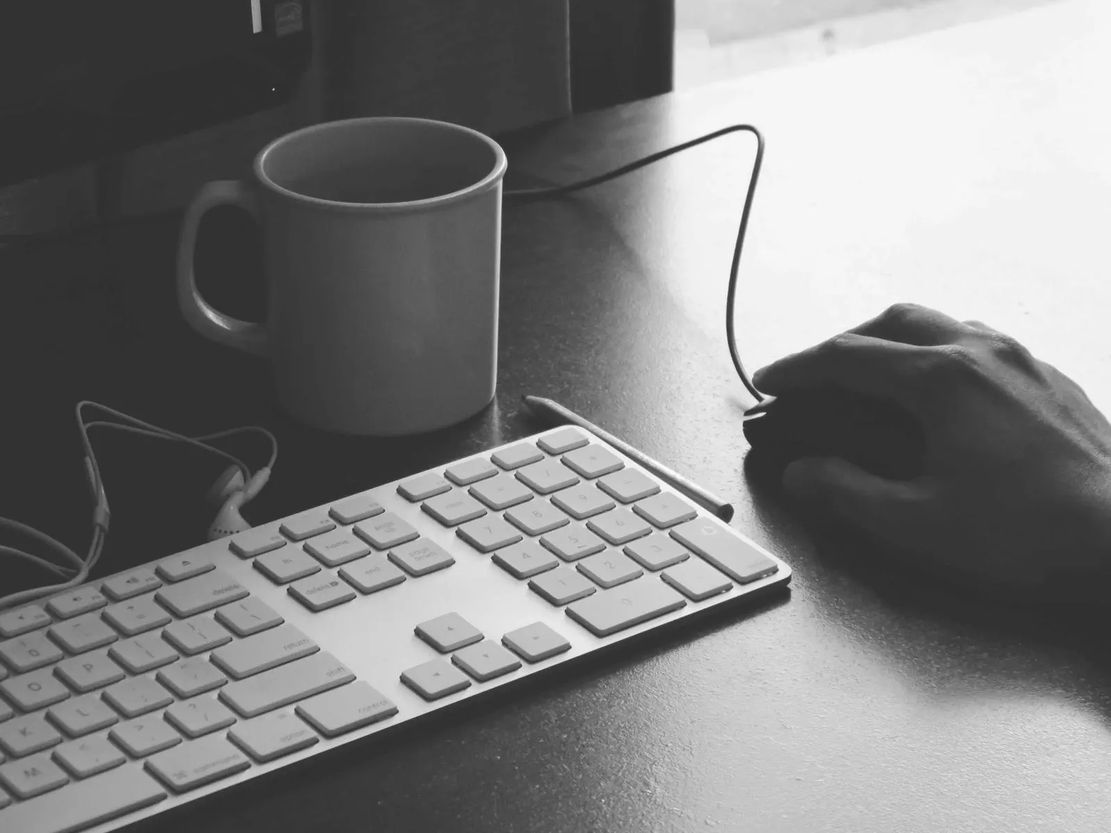 دست توسعه‌دهنده روی موس کنار کیبورد و فنجان قهوه در حال نوشتن Dockerfile